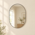 Oval metal-framed wall mirror hanging on a warm cream wall