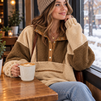 A woman in the color block sherpa sweatshirt sitting at a cozy cafe window with a latte